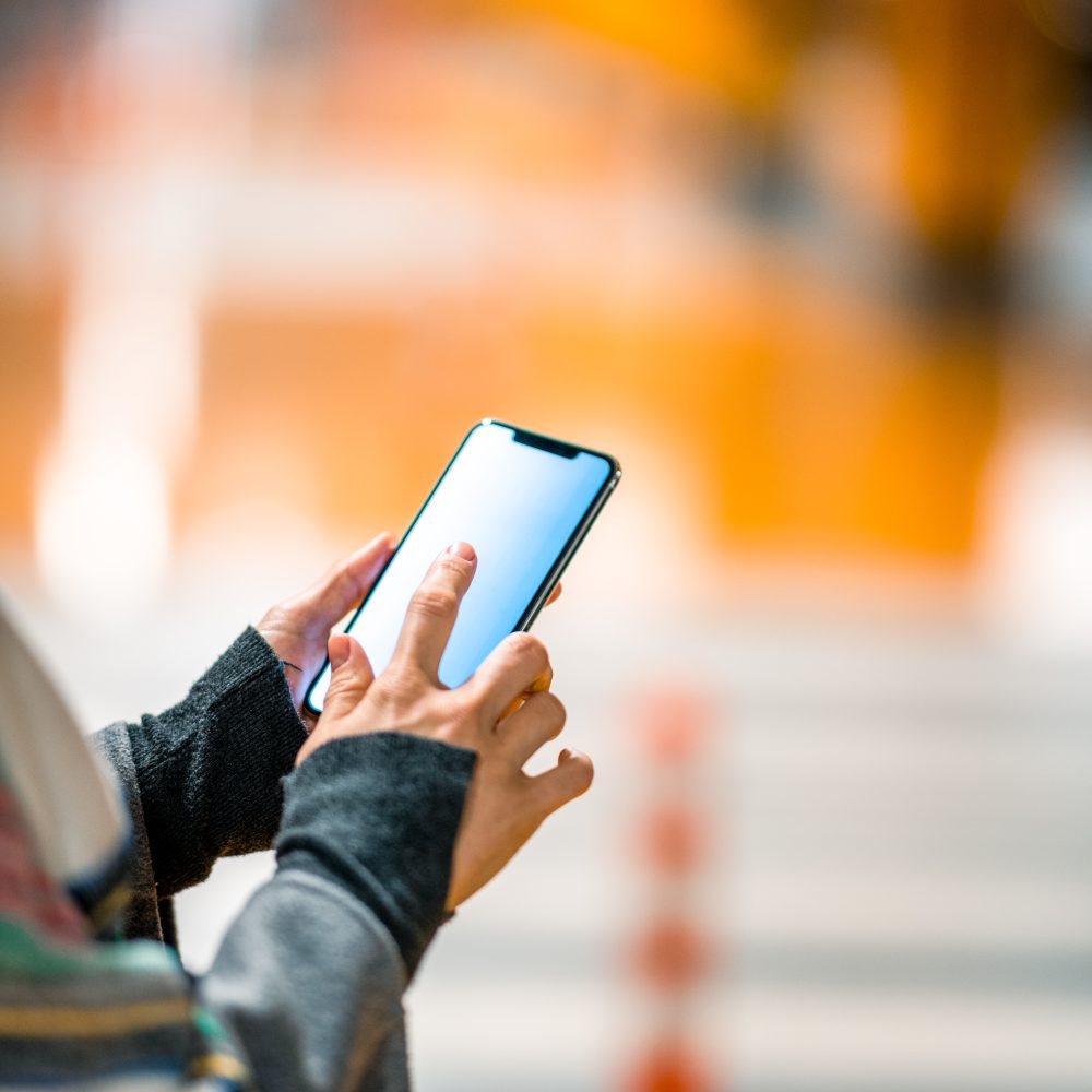 Businesswoman tapping on her cell phone application connected to her car in the garage of her working place.